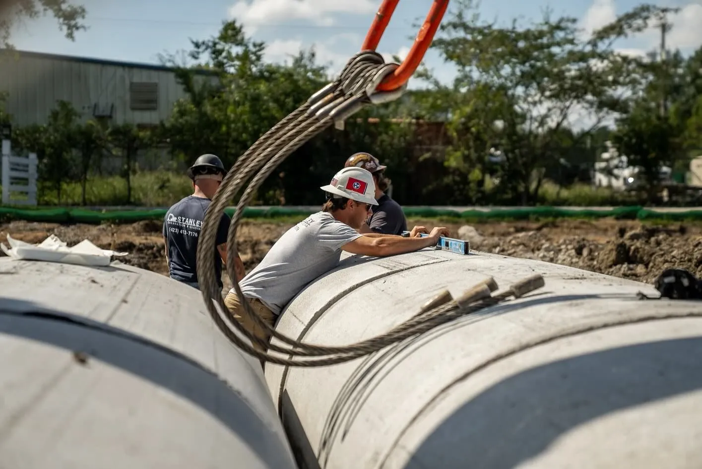 Construction workers aligning concrete pipes with a crane in a trench.