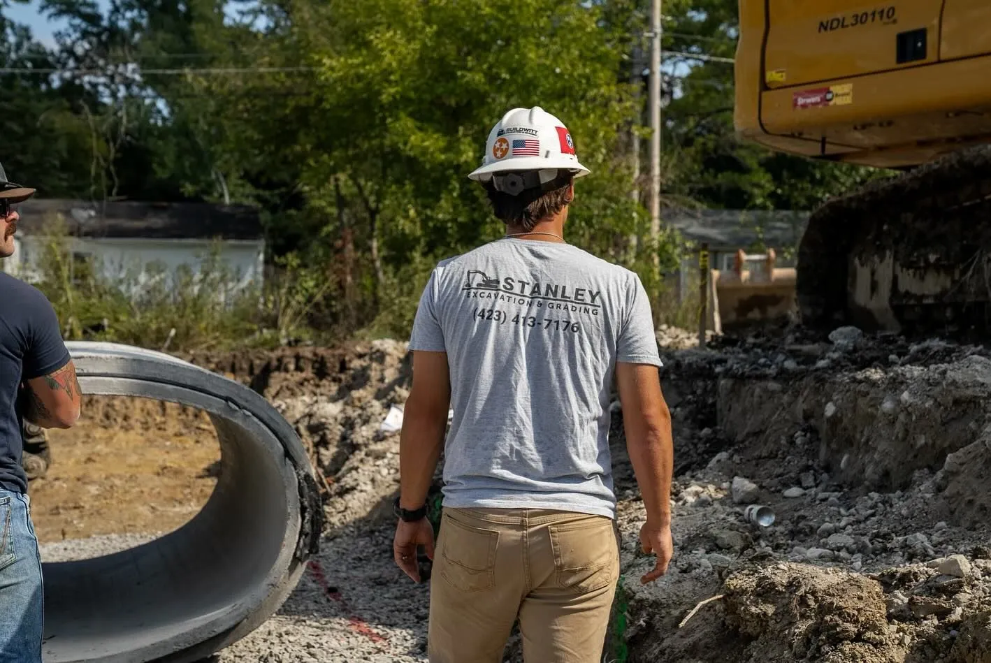 Construction worker in hard hat inspecting large pipe at a worksite.