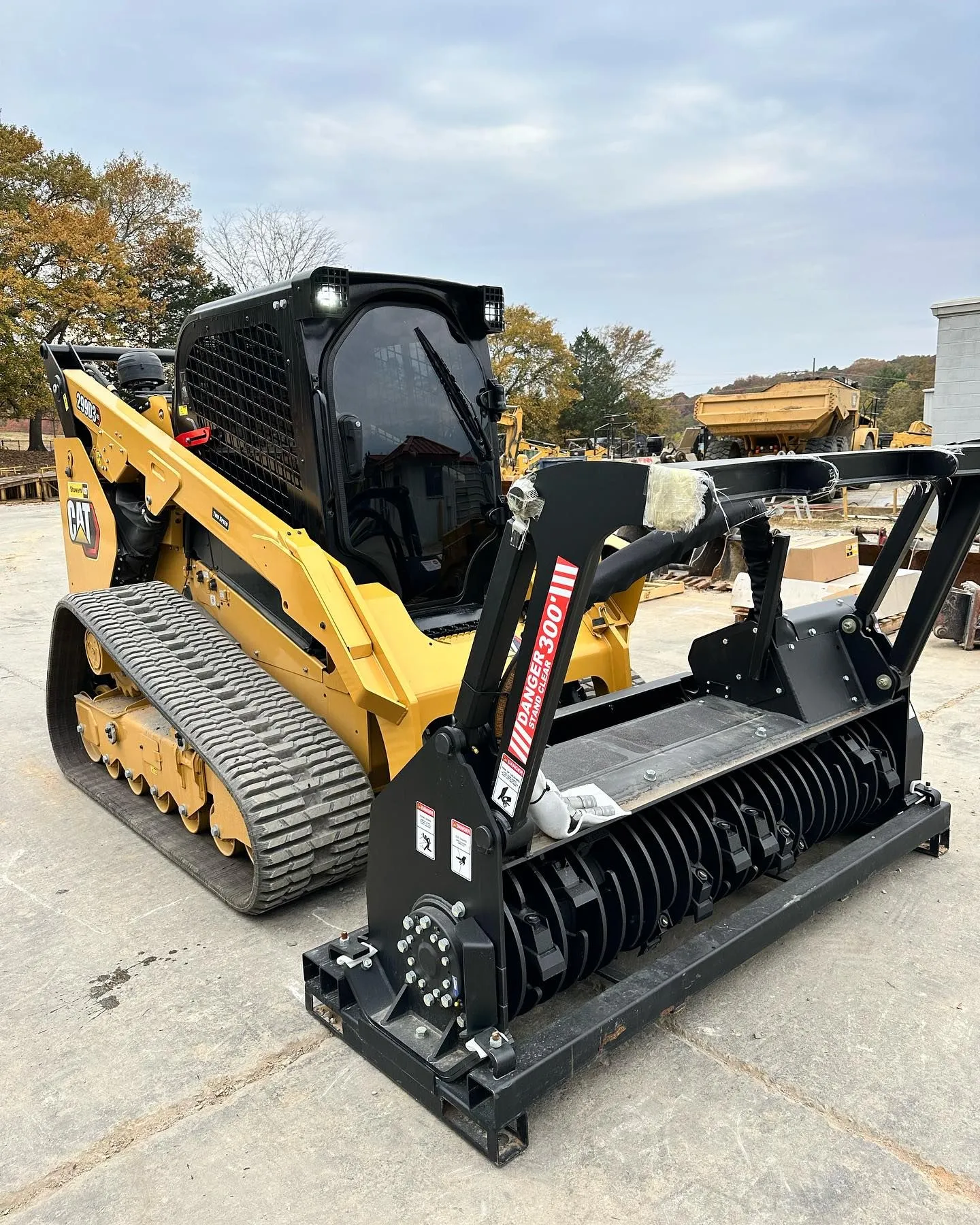 Yellow track skid steer with black forestry mulcher attachment outdoors.