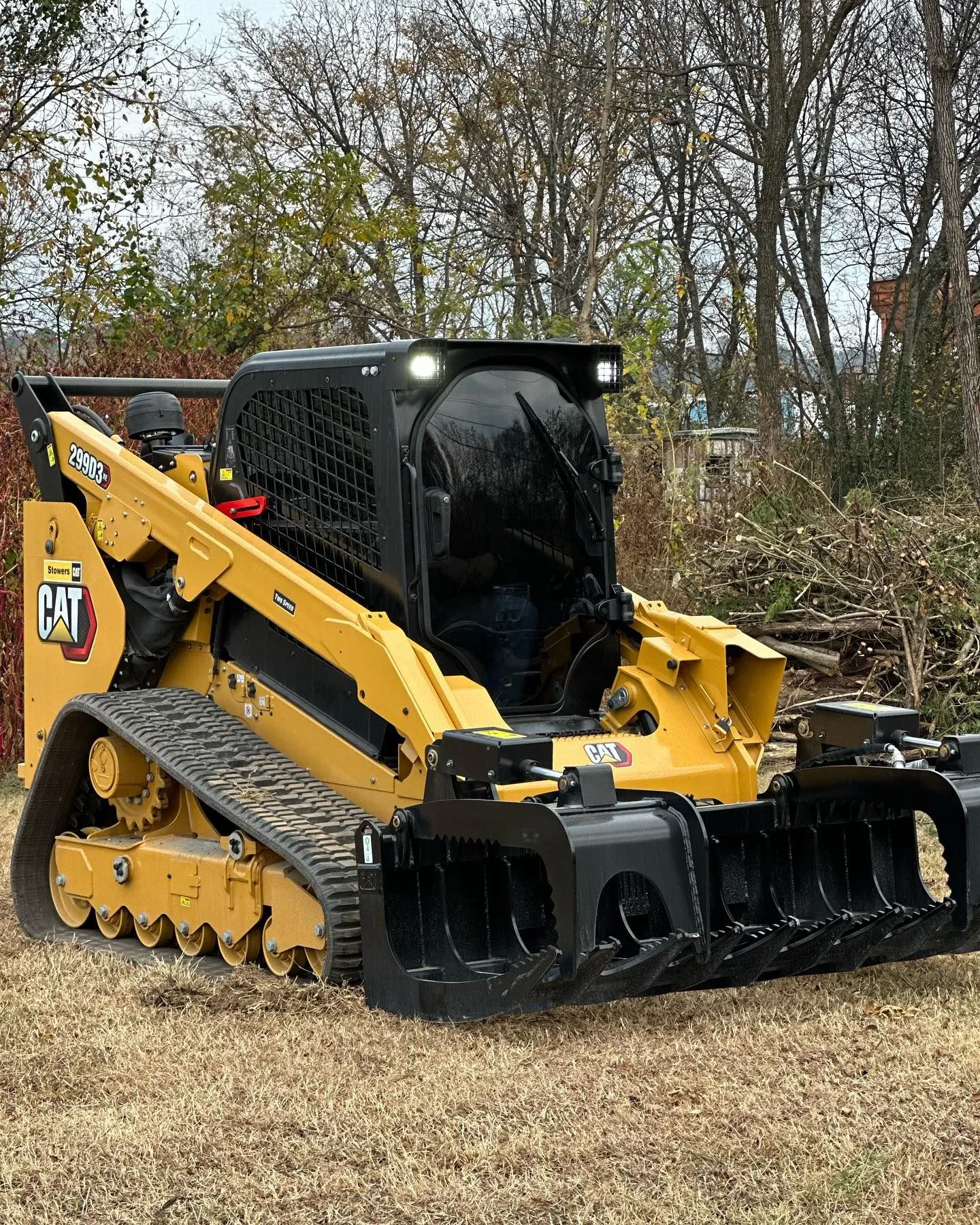 Yellow Caterpillar skid steer loader with black attachments, tracks, and a protective cage, in a grassy area.