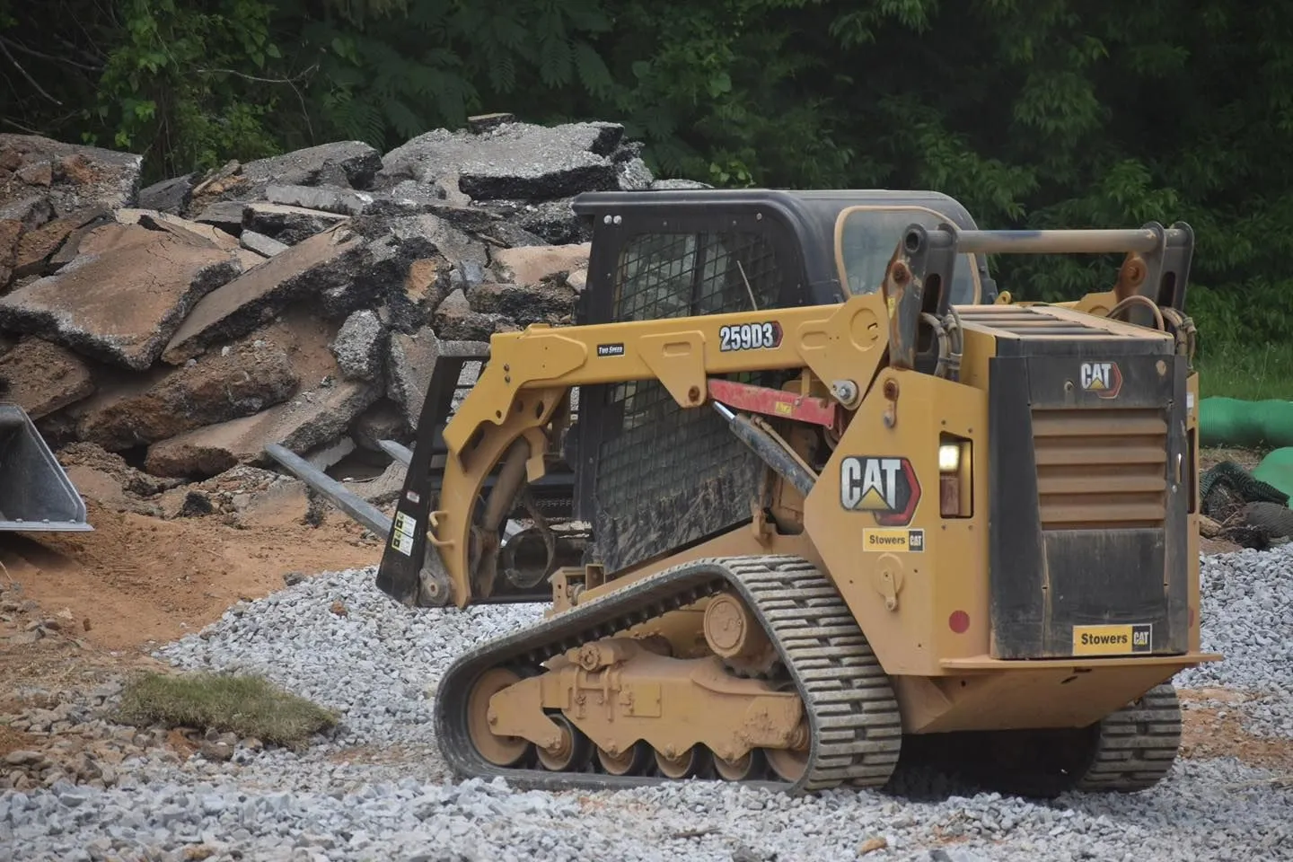 Yellow Caterpillar skid steer tracks on a construction site with pile of broken asphalt.