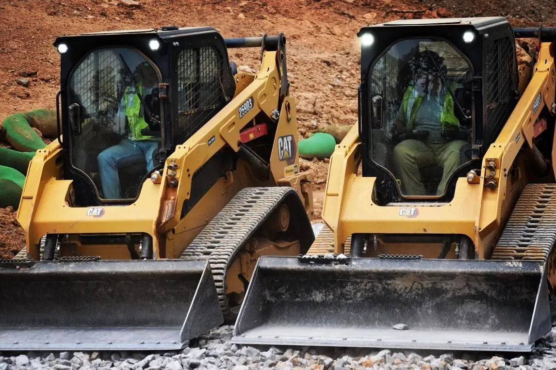 Two yellow skid steer loaders with operators at a construction site.