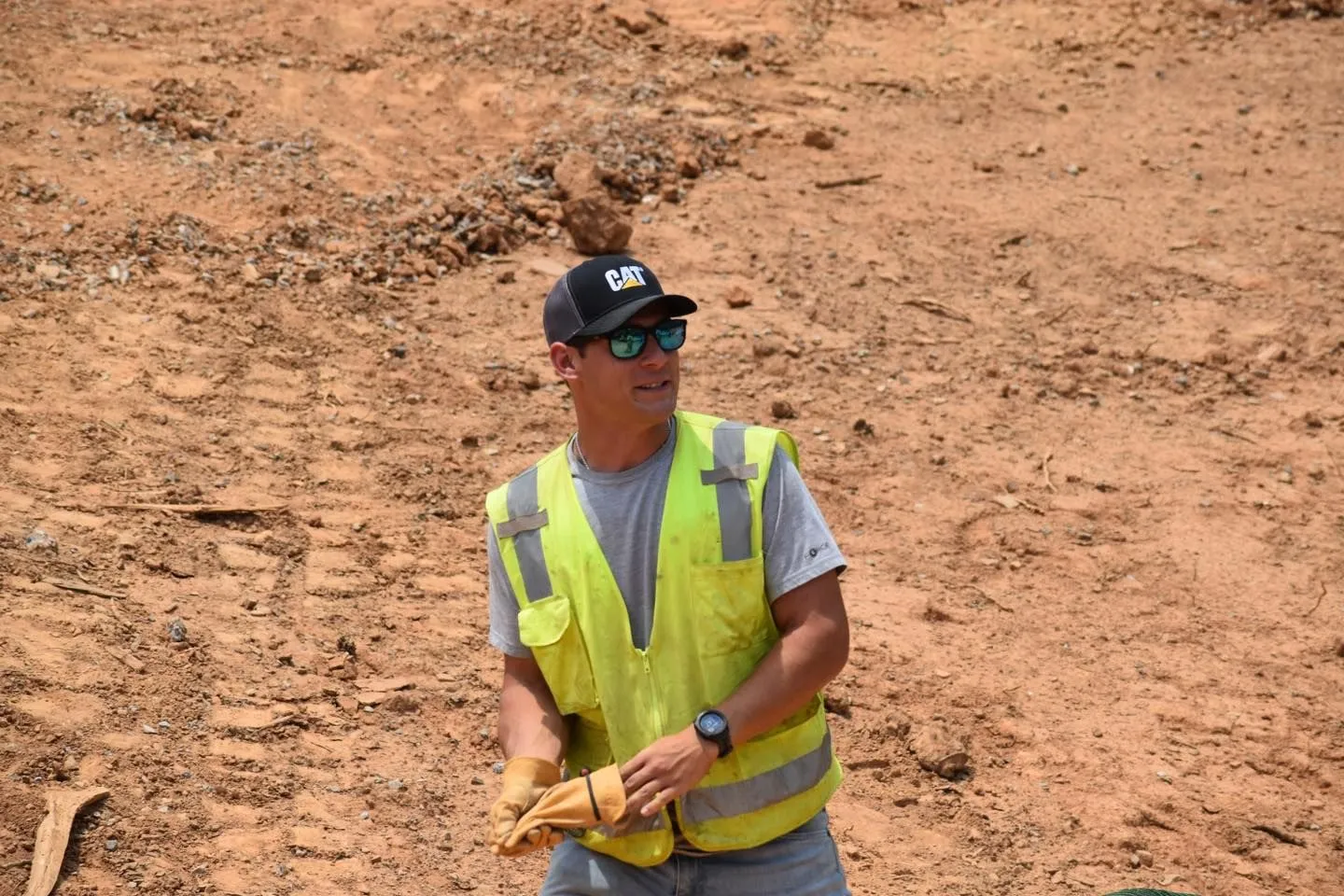 Man in yellow vest and cap on a construction site, looking away.