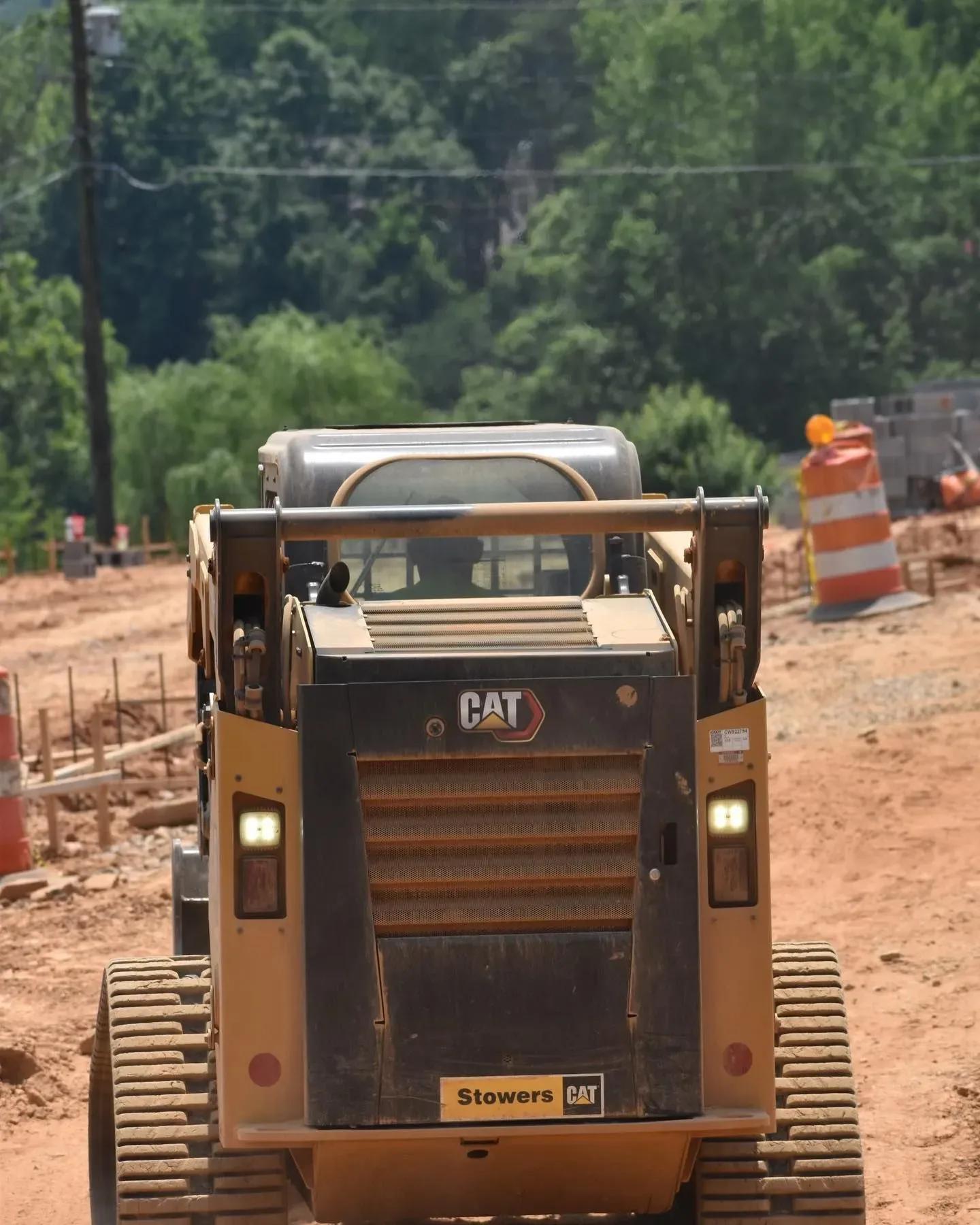 A yellow CAT skid steer on a construction site with trees and an orange traffic cone in the background.