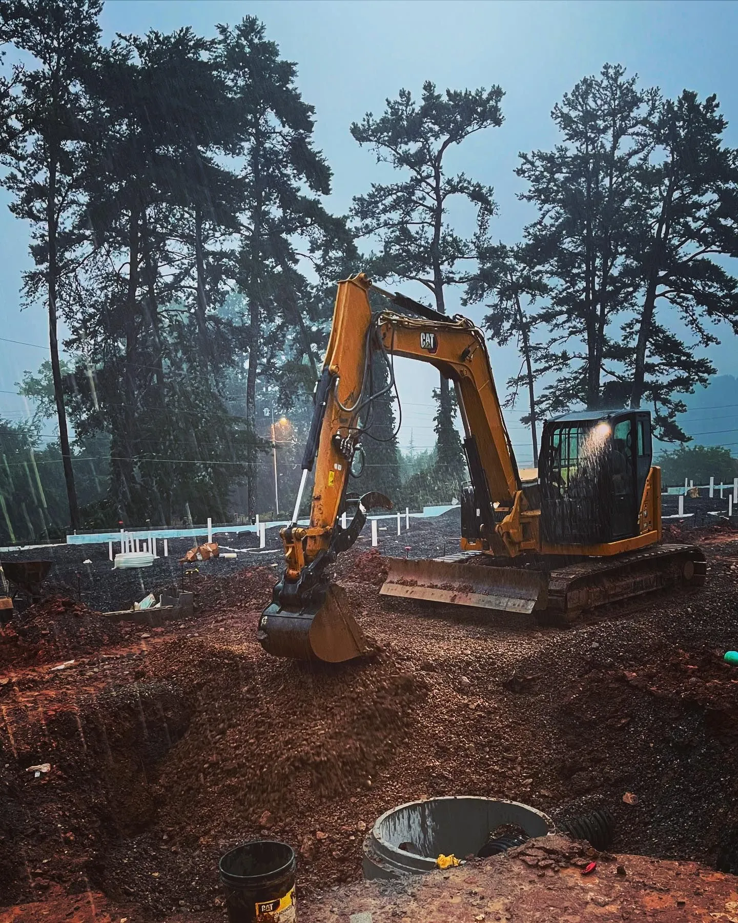 Cat excavator digging a storm drainage basin in the rain on a construction site
