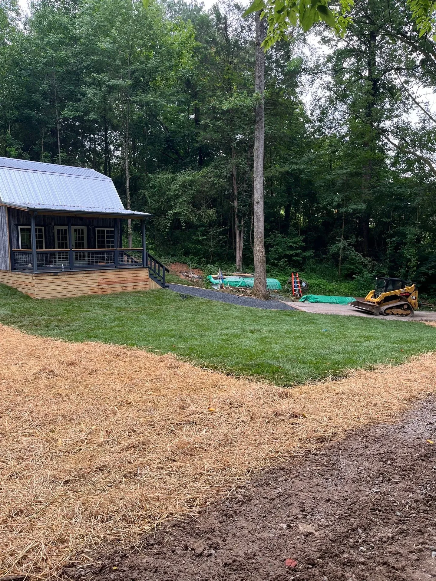 Cat track loader finishing a graded gravel path and new lawn behind a cabin