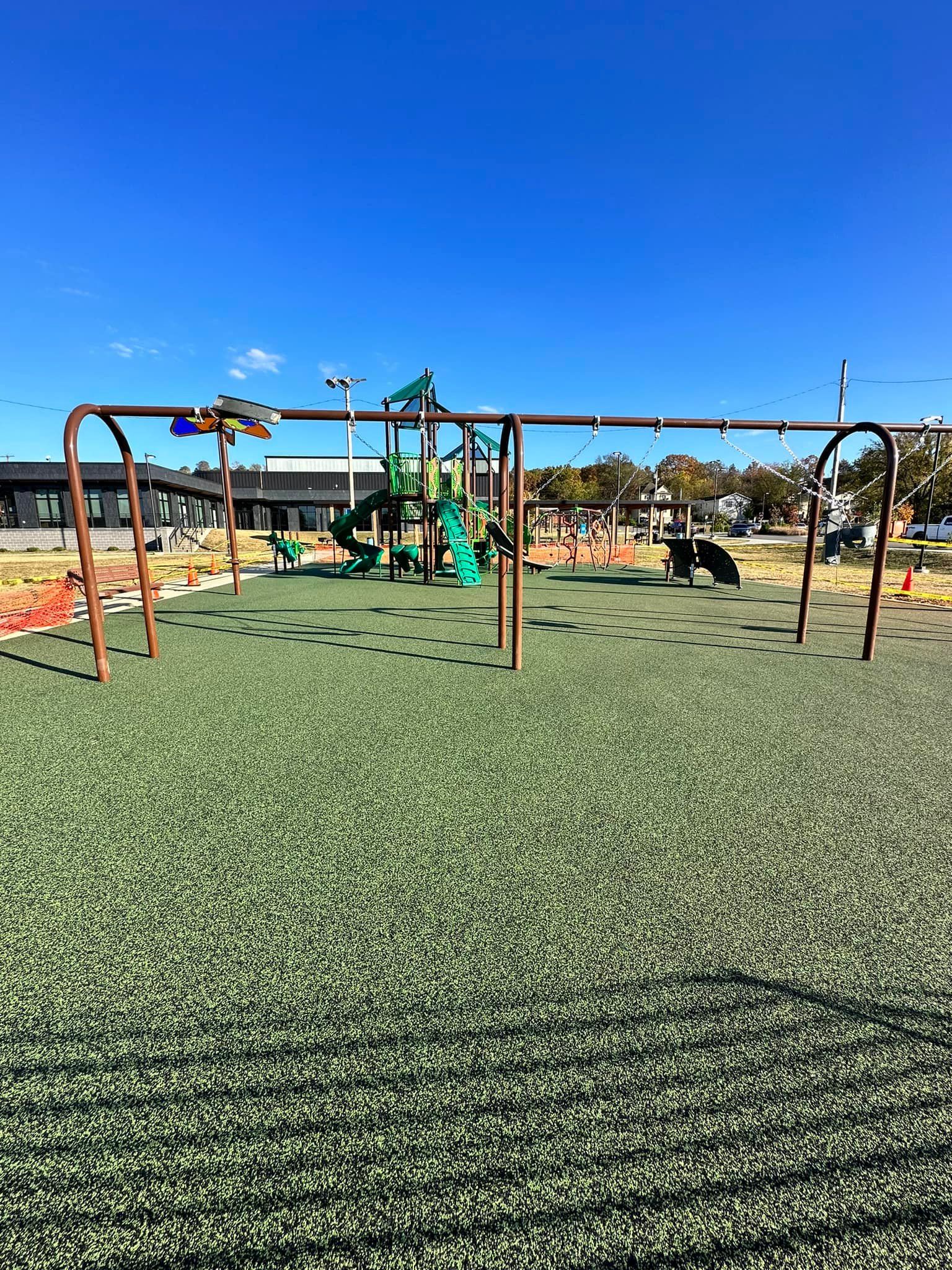Playground with swings, green turf, and play structure against a blue sky.