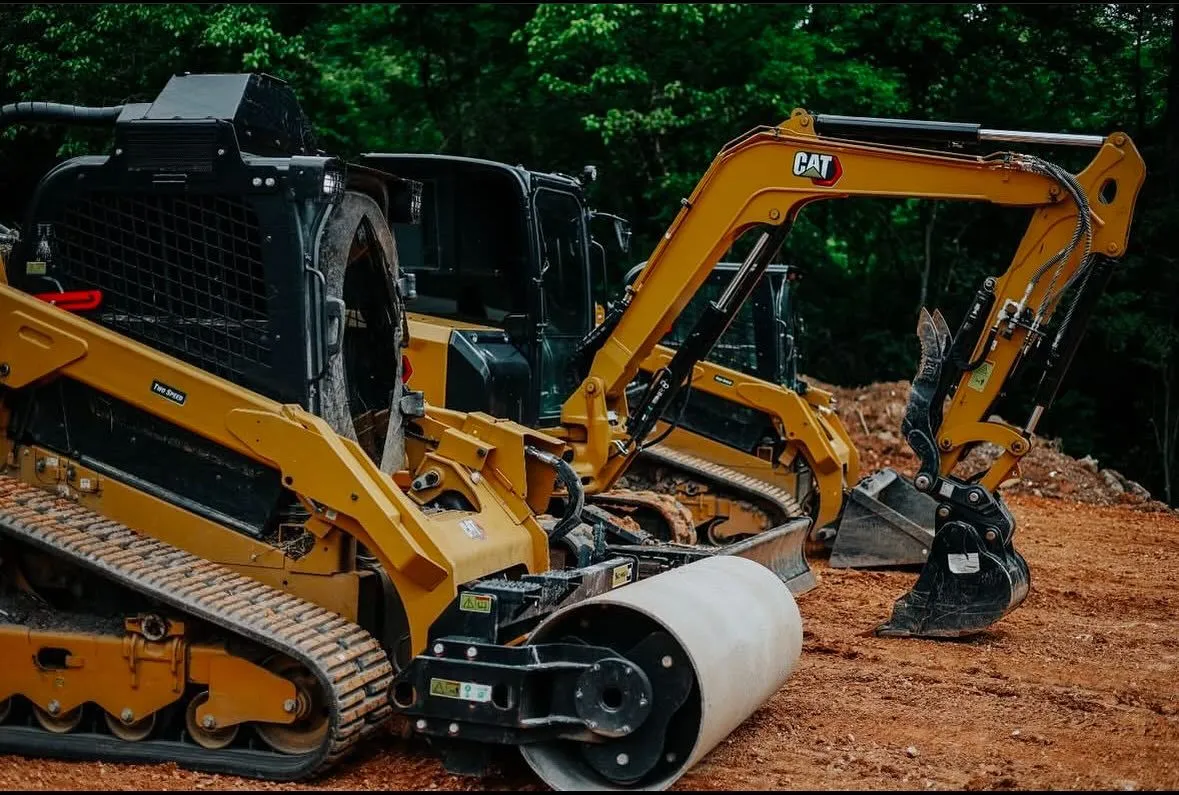 Yellow Caterpillar construction equipment on a dirt pile, with forest background.