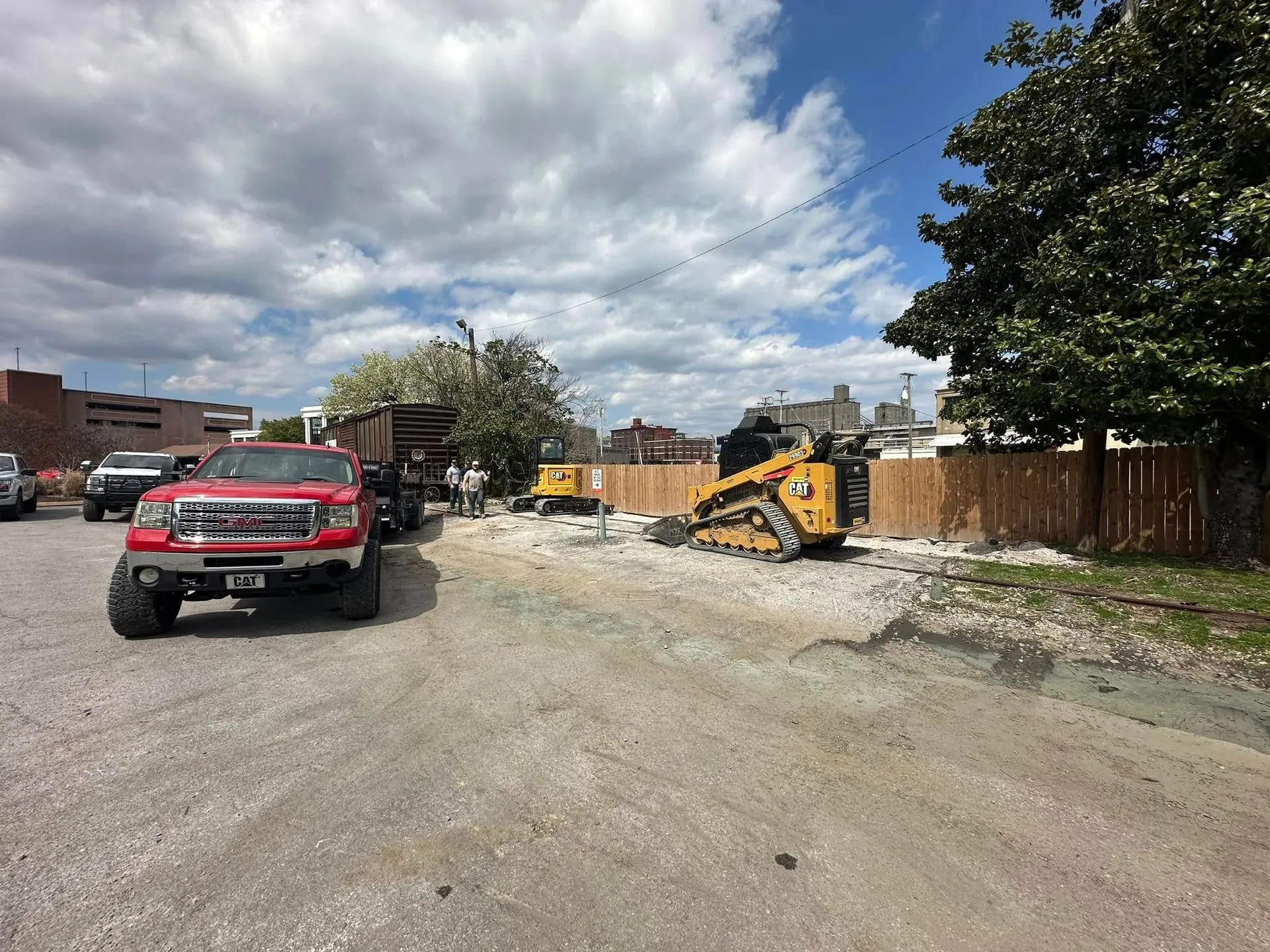 Construction site with a red truck, a yellow skid steer, and a dump truck under a cloudy sky.