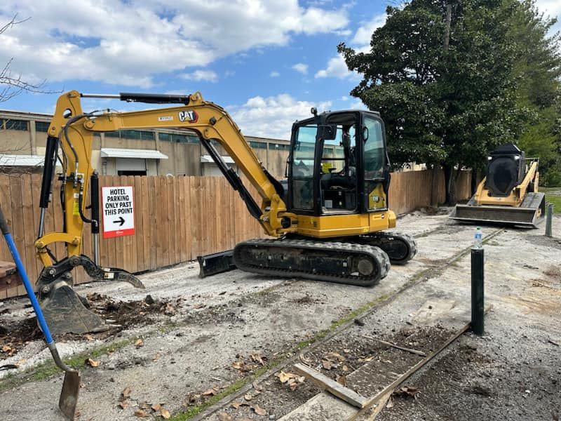 Cat mini excavator and skid steer breaking up an old parking area beside a wooden fence