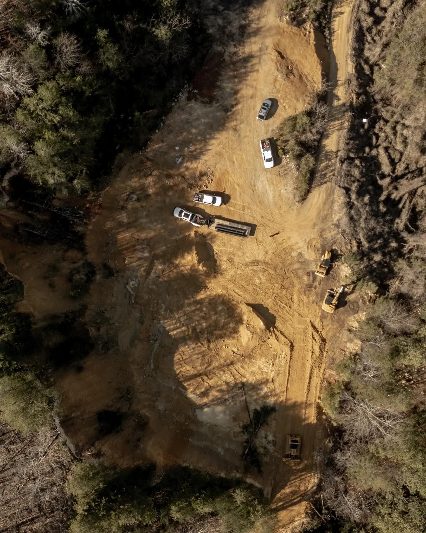 Aerial view of a cleared area in a forest with vehicles, including trucks and machinery, and construction activity.