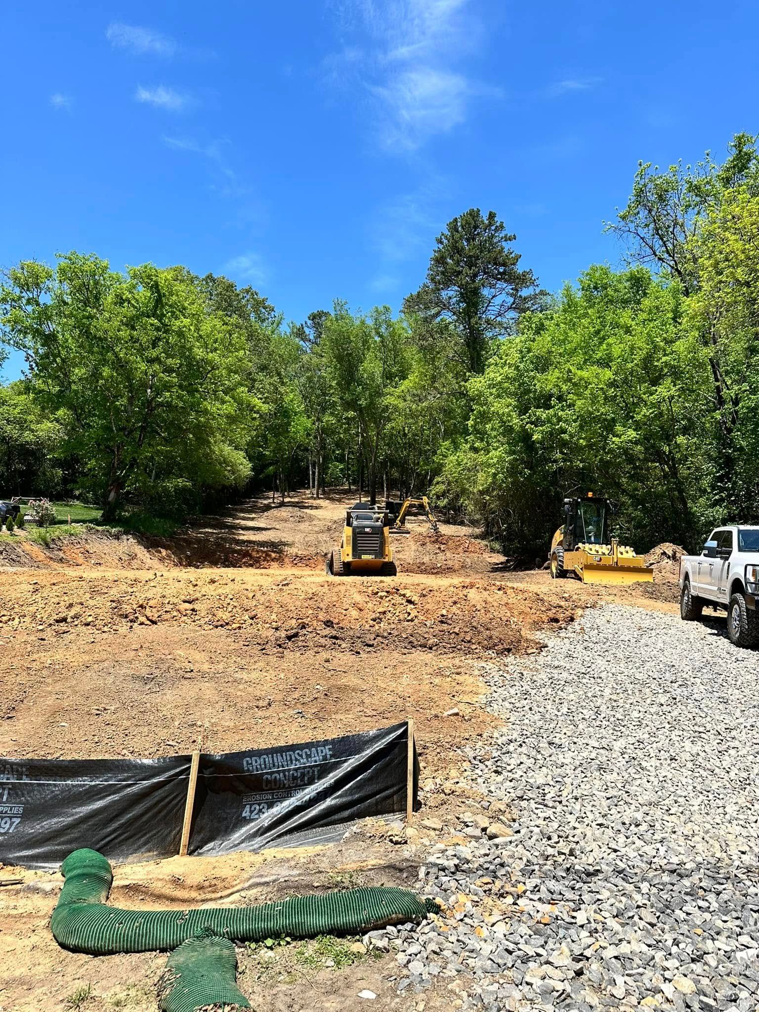 Construction site with bulldozer, dirt, rocks, and trees under a blue sky.