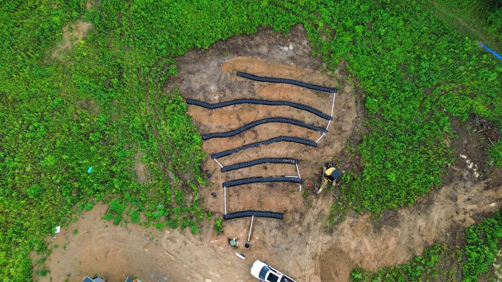 Overhead view of a person working in a garden bed with black landscape fabric creating curved rows surrounded by green grass.