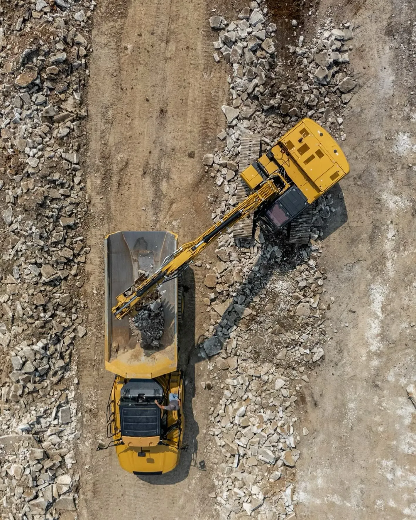 Aerial view of a yellow excavator loading debris into a dump truck.