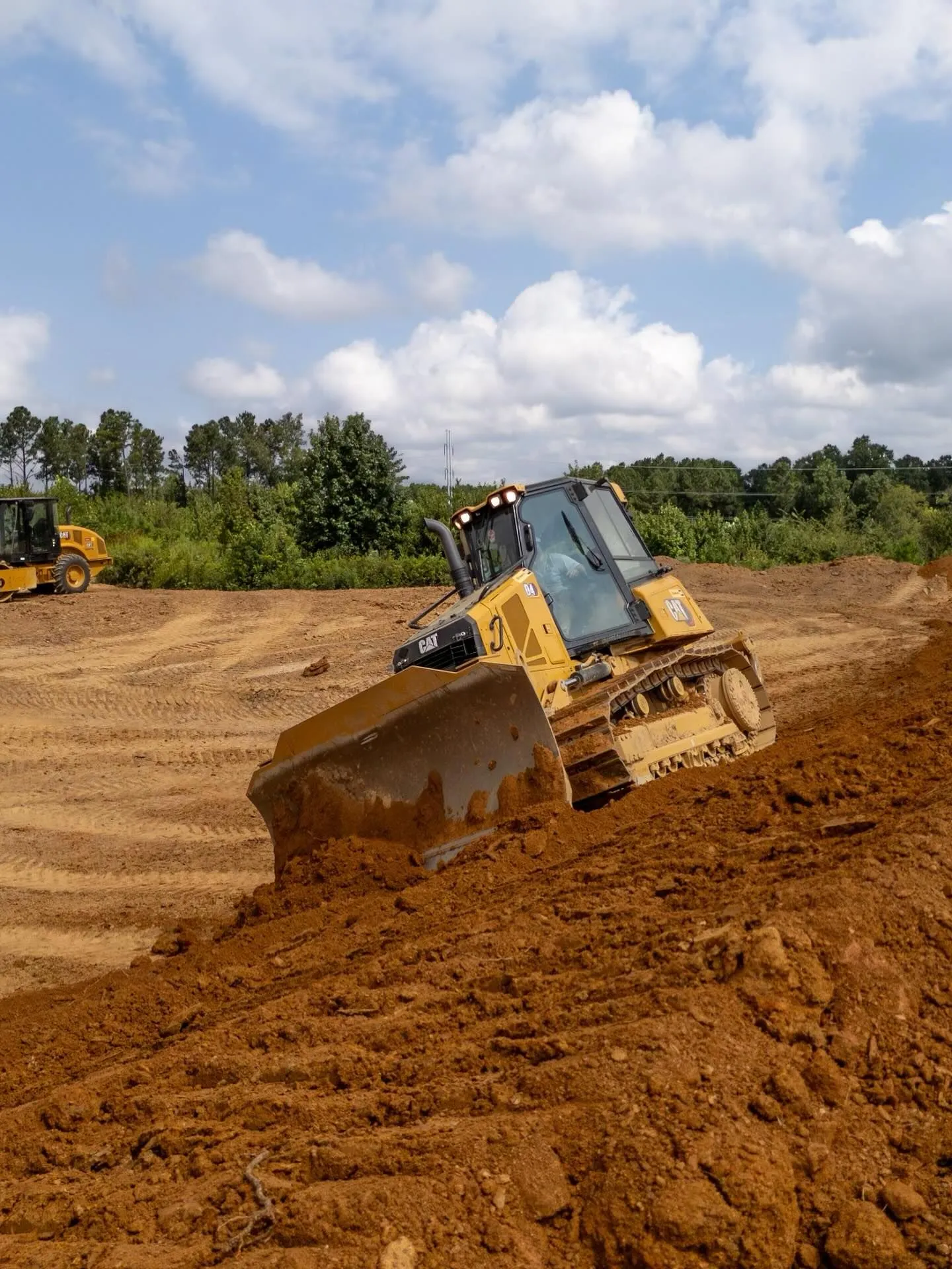 Cat D4 dozer grading red clay on a building pad while a compactor works in the background