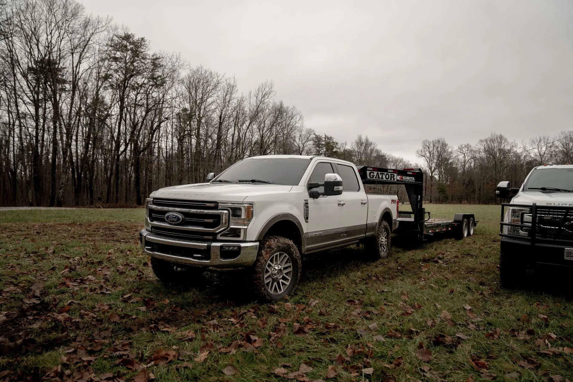 White pickup truck with a trailer parked in a grassy field on a cloudy day.