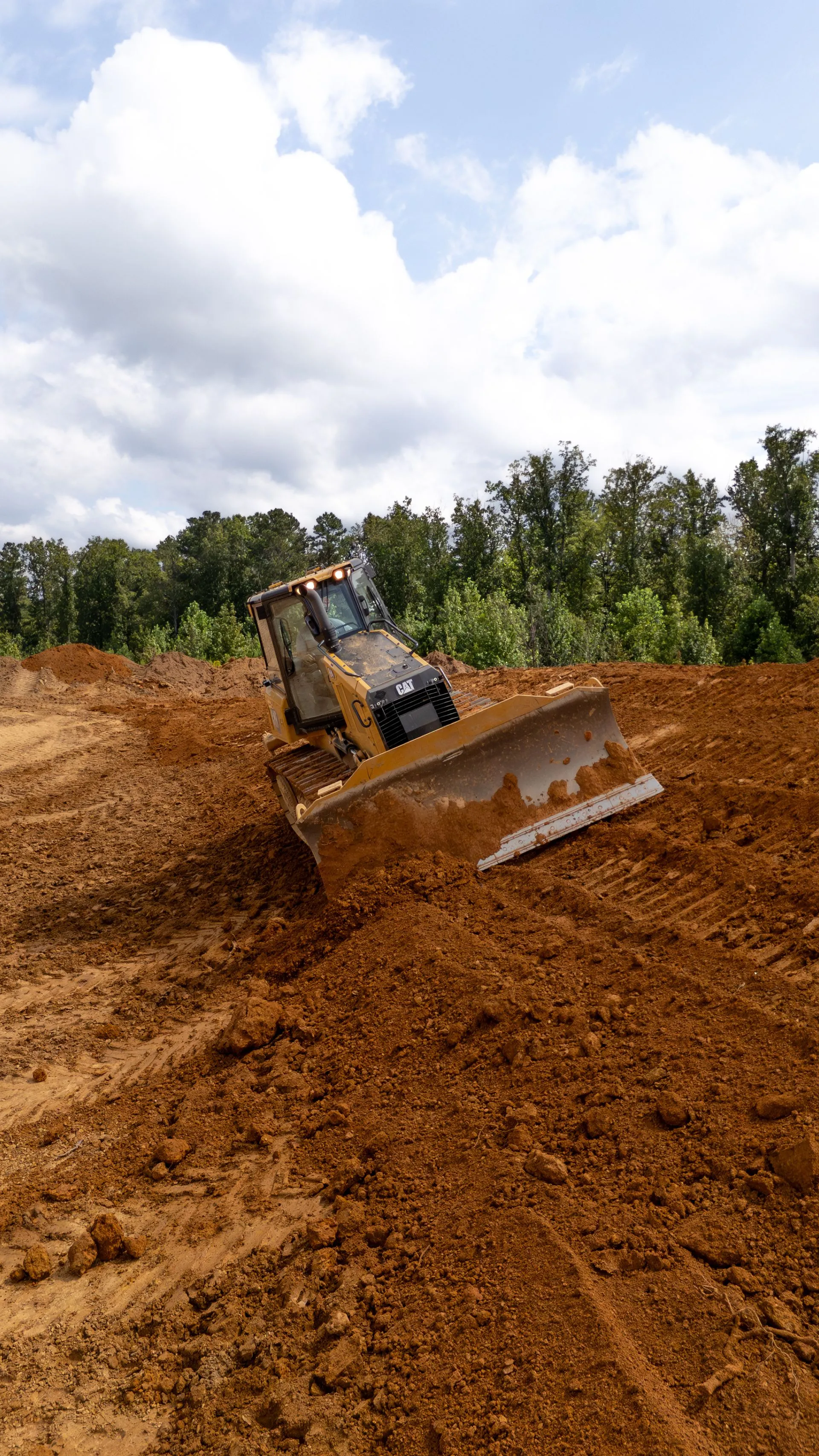 Cat dozer pushing red dirt while grading a home site, trees in the background