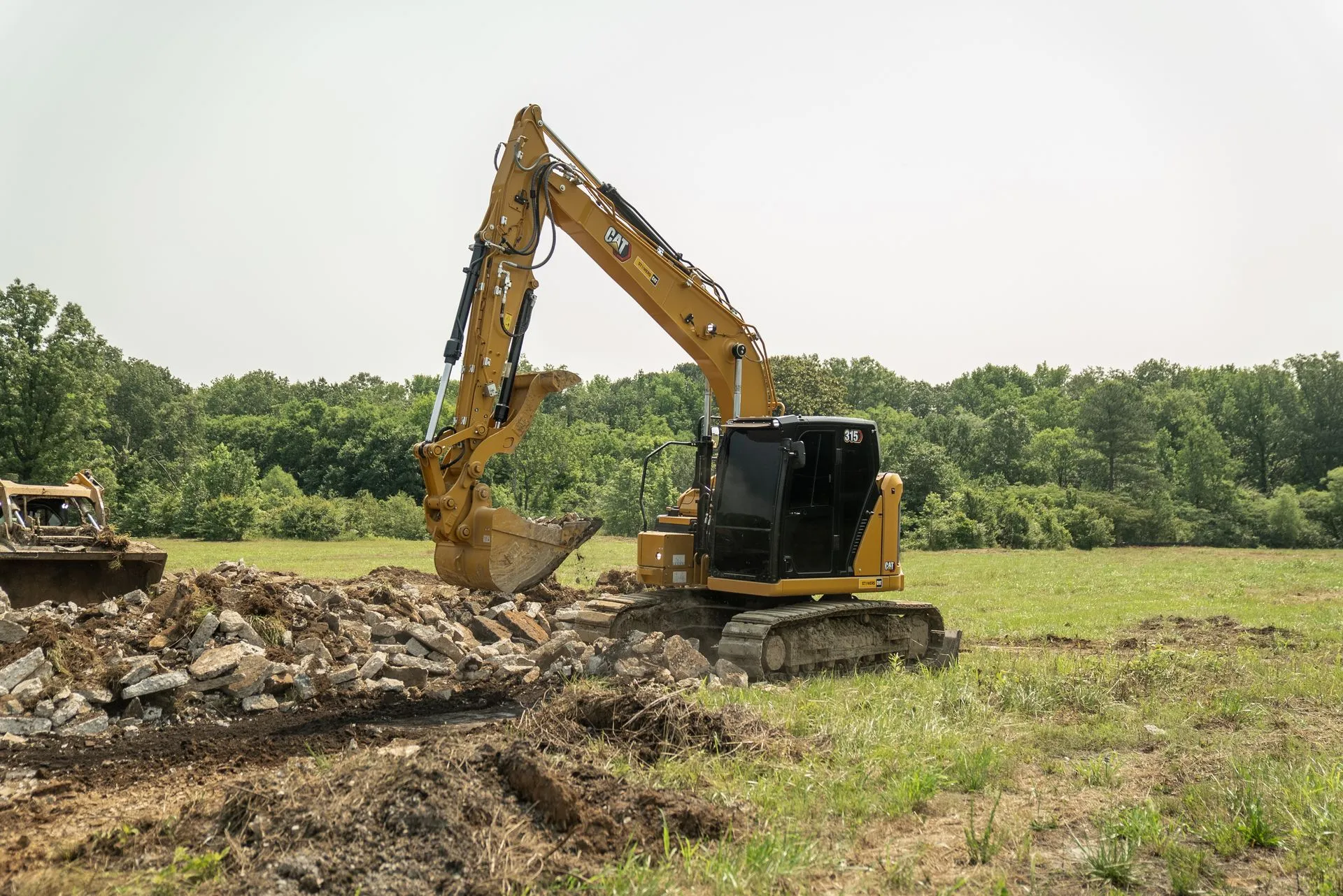 Yellow excavator digging earth in a field with trees in the background under a sunny sky.
