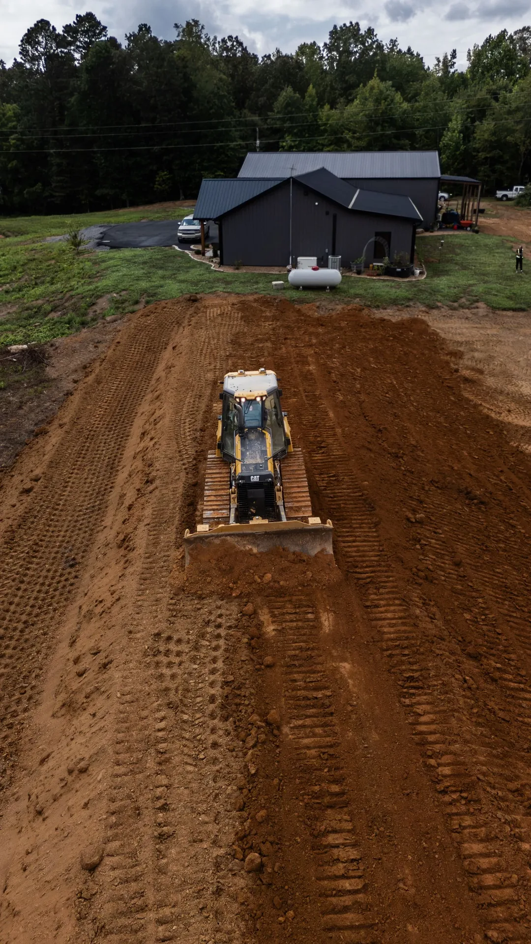 Bulldozer grading a brown field in front of a gray building.