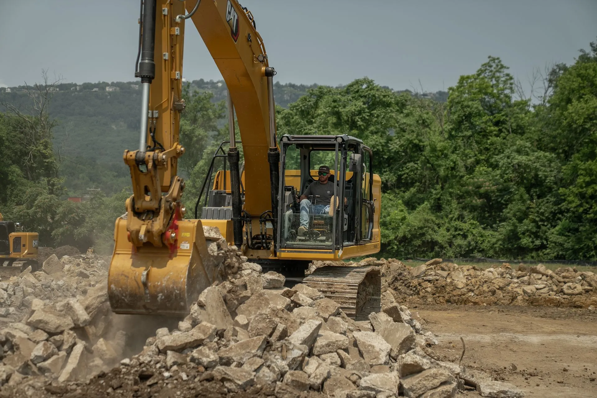 Yellow excavator scoops up concrete rubble in outdoor setting with trees.