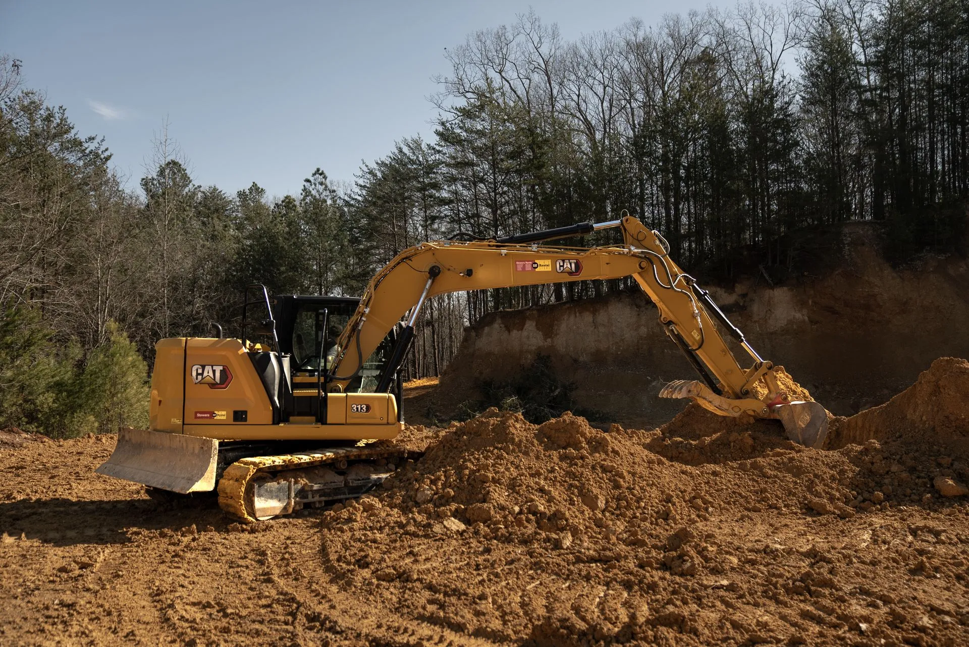 Yellow Caterpillar excavator digging in a dirt pile, forest background.