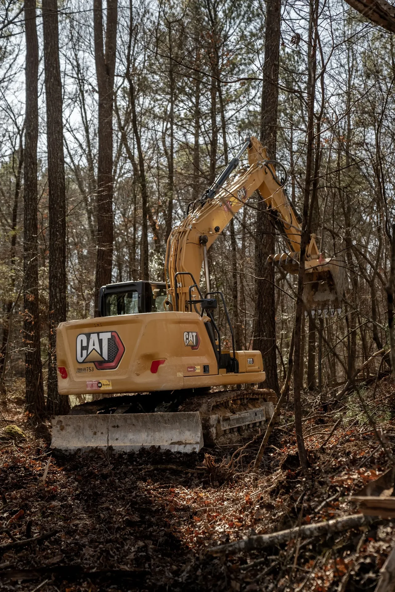 Yellow Caterpillar excavator in a wooded area, clearing trees.