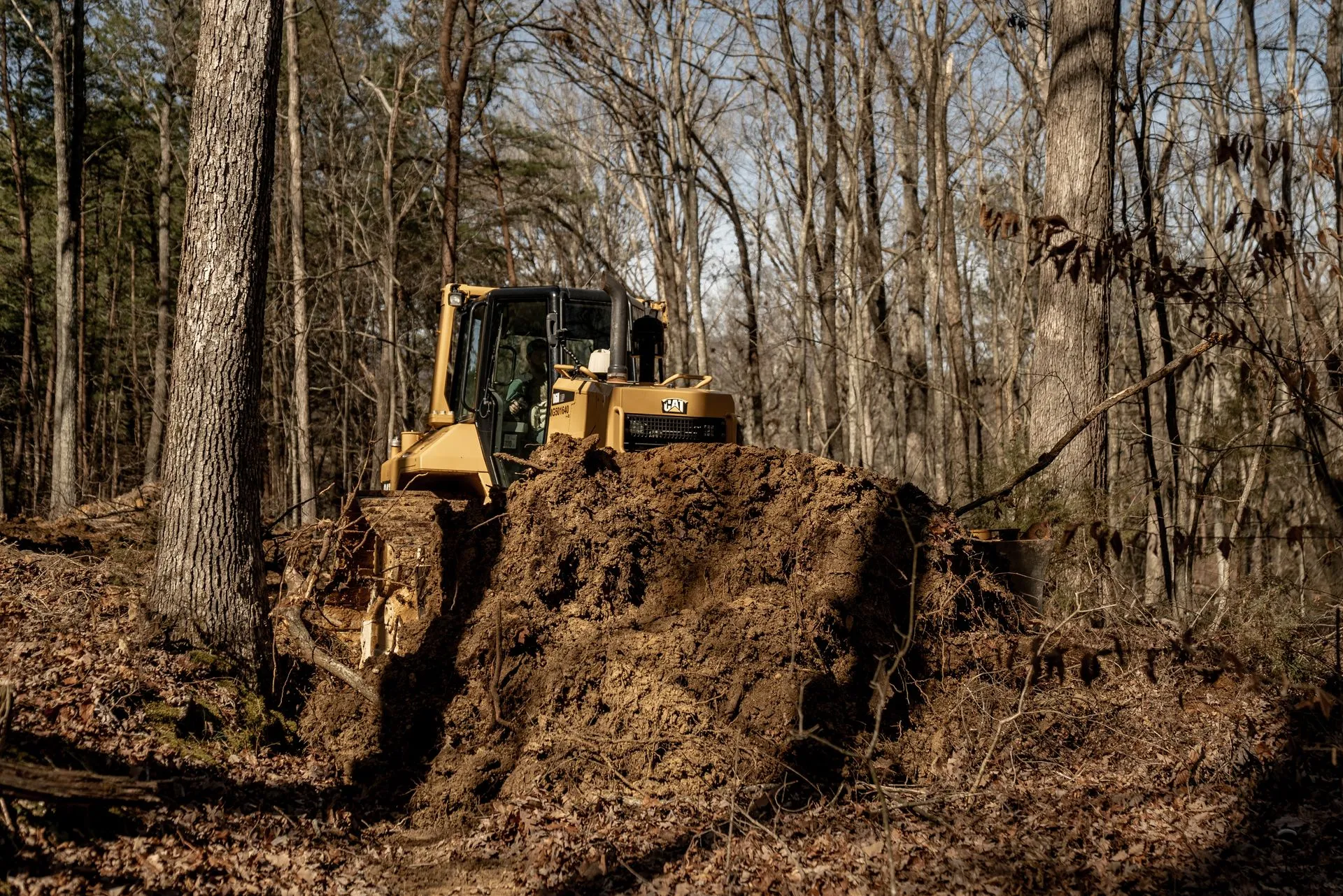 Yellow bulldozer pushing through a forest, clearing debris.